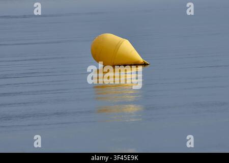 Une bouée marqueur jaune flotte en équilibre sur les eaux calmes et argentées de la mer, projetant un reflet doré vibrant à la surface. Le centré Banque D'Images