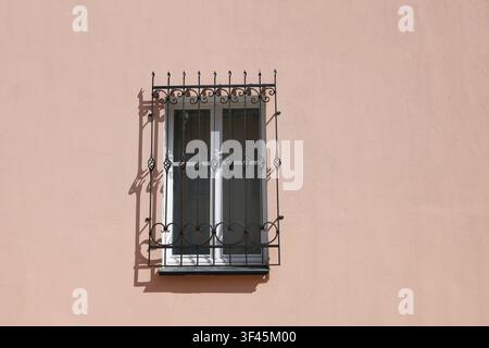 Barres de fenêtre en fer forgé sur fond mural rose photo. Grille de sécurité vintage en métal avec volutes décoratives projetant une ombre nette sur un mur texturé du bâtiment Banque D'Images