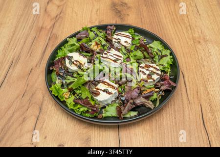 Médaillons de chèvre sur salade verte mélangée avec une drizzle de balsamique, noix, raisins secs et graines de courge Banque D'Images