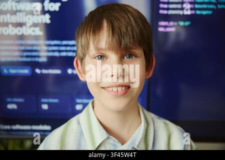Portrait d'un garçon caucasien souriant à la caméra avec une interface de programmation en arrière-plan, représentant l'apprentissage précoce des STEM et les compétences numériques. Utile pour la technologie éducative, les cours de programmation, l'innovation juvénile Banque D'Images