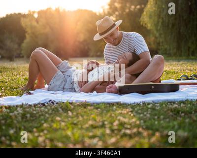 Baigné dans la douce lueur du coucher de soleil, un couple souriant profite d'un moment calme ensemble, entouré par la nature. Banque D'Images