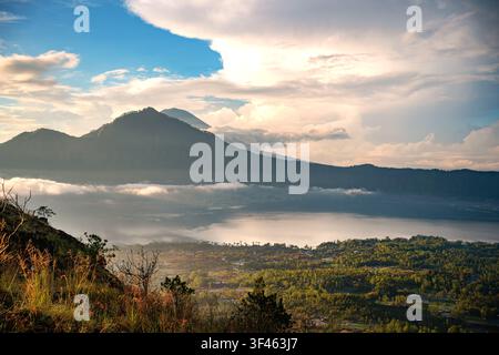 Lever de soleil doré illuminant le mont Batur et le lac Batur à Kintamani, Bali, Indonésie avec des nuages, des reflets et un paysage volcanique. Banque D'Images