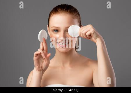 Joyeux jeune femme couvrant oeil avec tampon de coton, fond gris Banque D'Images