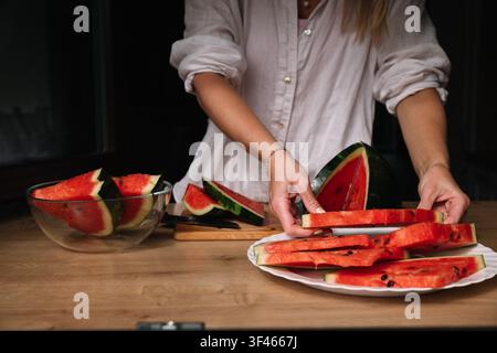 Couper et servir de la pastèque fraîche sur une table en bois dans une cuisine chaleureuse Banque D'Images