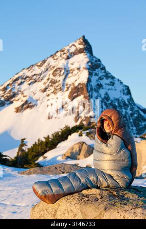 Femme heureuse assise dans un sac de couchage dans la neige Banque D'Images