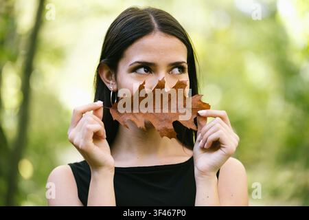 Jeune femme tenant un feuille brune à sa bouche de manière ludique Banque D'Images