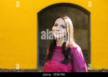 Jeune femme heureuse souriant devant un mur jaune vif Banque D'Images