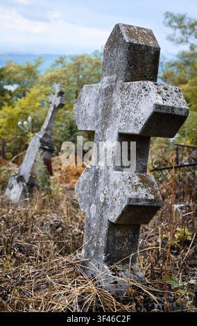 Une photographie verticale à faible angle d'un vieux croissant de pierre érodé penché dans un cimetière envahi par la végétation. Le monument fortement texturé est couvert de lichens Banque D'Images