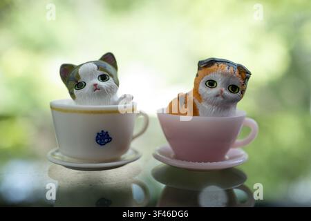 Chiang Mai, Thaïlande - 25 juillet 2026 : Deux figurines de chats dans des tasses à thé blanches et roses côte à côte, ornements de chatons calico et orange Banque D'Images