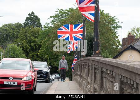 Maidenhead, Berkshire, Royaume-Uni. 27 juillet 2026. Un motard de la Thames Valley Police passe devant des drapeaux Union Jack récemment installés illégalement par des personnes inconnues sur les lampadaires du pont historique classé Grade I de Maidenhead sur l'A4 au-dessus de la Tamise à Maidenhead, Berkshire. La moitié du pont relève à la fois du Royal Borough of Windsor & Maidenhead (RBWM) et du Buckinghamshire Council. Le retrait proposé des drapeaux serait « coûteux et délicat », a déclaré le conseiller du RBWM Geoff Hill. Cela a suscité un émoi sur les réseaux sociaux. La section de Maidenhead de Re Banque D'Images