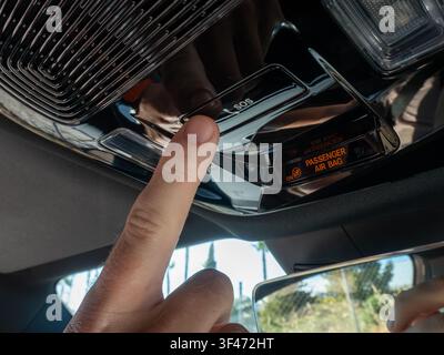 Présentation en gros plan de l'index d'un conducteur appuyant sur le bouton d'appel d'urgence SOS sur la console supérieure brillante d'une voiture de luxe moderne. L'image met en valeur Banque D'Images