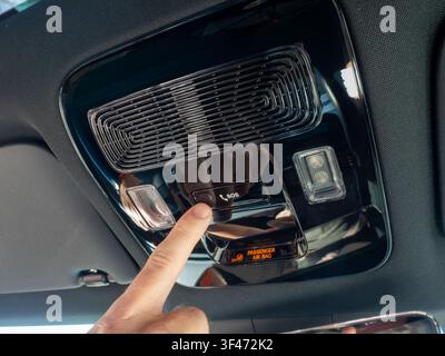 Présentation en gros plan de l'index d'un conducteur appuyant sur le bouton d'appel d'urgence SOS sur la console supérieure brillante d'une voiture de luxe moderne. L'image met en valeur Banque D'Images