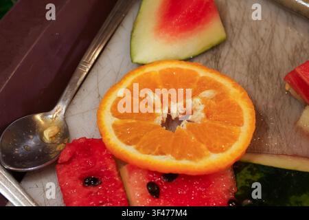 Une tranche d'orange et des morceaux de pastèque sur une planche à découper avec une cuillère montrant une collation fraîche aux agrumes et aux fruits d'été, couleurs vives et texture juteuse Banque D'Images