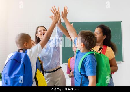 Enseignante enthousiaste donnant un high five aux écoliers devant le tableau noir de la classe Banque D'Images