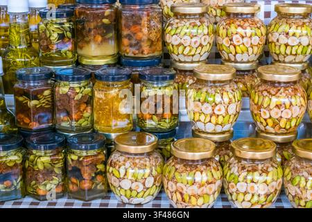 Variété de bocaux en verre remplis de noix et de fruits secs variés dans du miel doré, soigneusement disposés sur une étagère pour une présentation gastronomique. Banque D'Images
