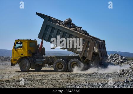 Un grand camion-benne jaune déchargeant du gravier et des roches dans une mine à ciel ouvert de cuivre, illustrant le processus industriel de l'exploitation minière du cuivre dans un environnement rude et Banque D'Images