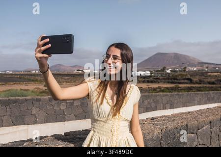 Une jeune femme prend un selfie devant le paysage volcanique époustouflant de Lanzarote, capturant le terrain unique et l'ambiance ensoleillée. Le fond rev Banque D'Images