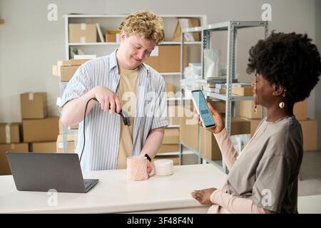 Homme adulte scannant un produit pendant qu'une femme noire paie par smartphone Banque D'Images