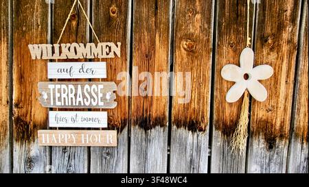 Panneau de bienvenue indiquant «Chez nous, c'est toujours l'heure du bonheur» sur un mur en bois patiné avec une fleur décorative, Suisse Banque D'Images