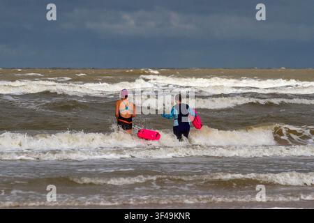 Une femme en maillot de bain une pièce noir et bleu et bonnet de bain violet se tient dans les vagues peu profondes d'une mer ouverte pendant une session de natation. Banque D'Images