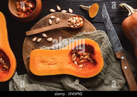 Vue de dessus de courge butternut crue avec cuillère en bois et graines sur planche à découper en bois. Des moitiés de citrouille se rapprochent. Photographie culinaire Banque D'Images