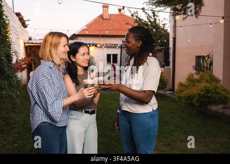 Amies femmes multiethniques portant un toast à leurs boissons dans l'arrière-cour Banque D'Images