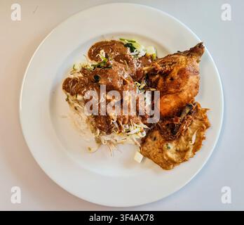 Vue de dessus de Nasi Pecel indonésien comprenant du riz cuit à la vapeur, des légumes, une sauce aux cacahuètes épicée et du poulet frit croustillant dans une assiette blanche. Banque D'Images