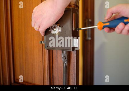 Mains de serrurier installant une nouvelle serrure de sécurité sur une porte en bois Banque D'Images