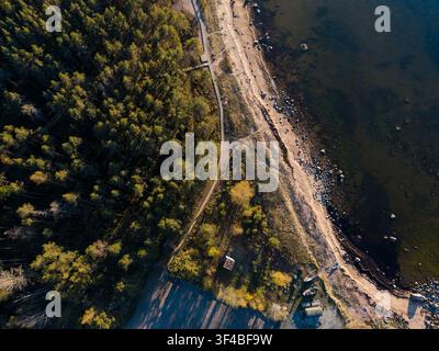 Vue aérienne de forêt de pins côtière et de plage de sable avec des bateaux et un sentier sinueux au coucher du soleil Banque D'Images