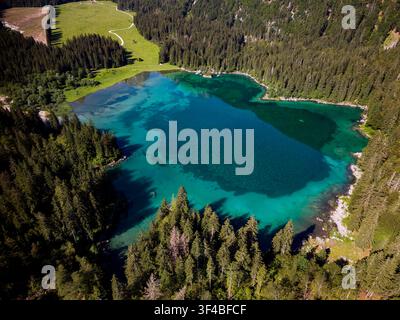 Vue aérienne d'un lac alpin turquoise entouré d'une forêt dense à feuillage persistant et d'un sentier de prairie Banque D'Images