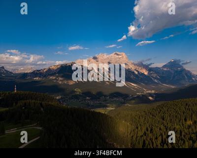 Vue aérienne d'une chaîne de montagnes alpines et d'une vallée boisée surplombant un petit village au coucher du soleil Banque D'Images