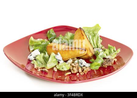 Salade avec poires caramélisées, noix et fromage bleu, sur une assiette rouge, isolée sur fond blanc Banque D'Images