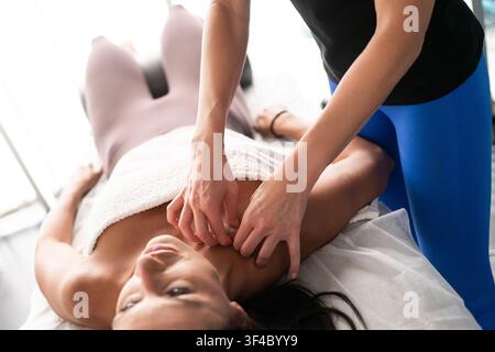 Femme adulte recevant un massage ciblé du cou et des épaules dans un studio de bien-être lumineux, le thérapeute exerce une pression douce sur le trapèze et la base du crâne Banque D'Images