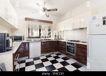Intérieur de cuisine moderne et lumineux avec des bas de placards en bois sombre brillant, des éléments supérieurs blancs et un sol carrelé noir et blanc à damier distinctif Banque D'Images