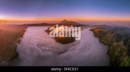 Vue panoramique aérienne du Mont Bromo en éruption au lever du soleil avec le Mont Batok, le Mont Semeru et une mer de nuages dans le parc national de Bromo Tengger Semeru, Est Banque D'Images