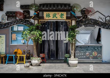 Une prise large montre l'entrée d'un restaurant chinois traditionnel avec un rideau de porte en plastique sombre sous une enseigne en bois portant des caractères chinois verts Banque D'Images