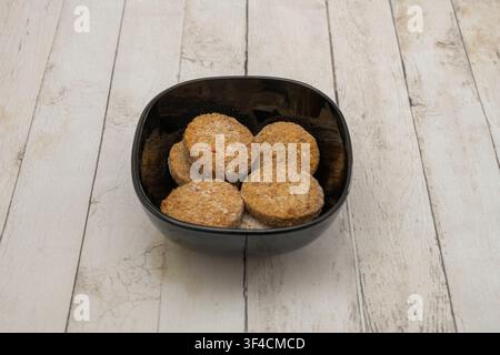Gros plan de disques de falafel panés et croustillants servis dans un bol noir sur une surface en bois blanchâtre. Banque D'Images