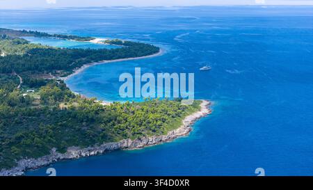 Une vue par drone montre une péninsule boisée bordée par une côte rocheuse et des criques turquoise vives, s'étendant dans les eaux bleu profond près de Golden Beach, en Grèce. Banque D'Images
