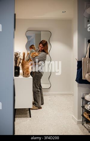 Femme tenant un chat debout dans un couloir moderne avec miroir et décoration Banque D'Images