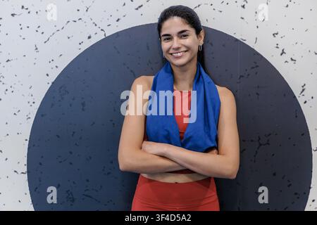 Une femme fait de l'exercice dans une salle de sport. Elle se tient avec confiance, les bras croisés, et sourit. L'entraînement fait partie de sa routine de fitness. L'environnement de la salle de sport Banque D'Images
