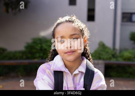 Adolescent afro-américain debout dans une cour face à la caméra, portant une veste à carreaux et un sac à dos Banque D'Images