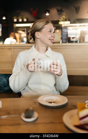 Une femme savoure une boisson chaude dans un café en après-midi dans une atmosphère chaleureuse avec une décoration simple Banque D'Images
