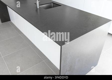 Une île de cuisine élégante avec un plan de travail noir contrasté et des lignes épurées met en valeur la décoration contemporaine Banque D'Images