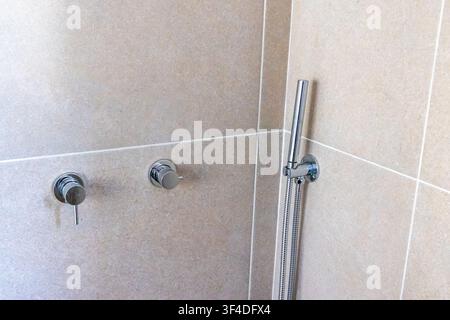 Une vue rapprochée de robinets de douche chromés élégants sur un fond de carreaux neutres Banque D'Images