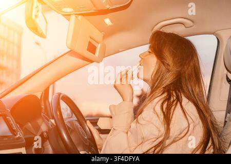 Maquillage de voiture pour femme appliquant du rouge à lèvres dans le véhicule pendant l'heure dorée au coucher du soleil tout en étant assise sur le siège du conducteur Banque D'Images