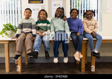 Écoliers afro-américains assis sur un banc en bois dans une salle de classe avec des affiches MATH Banque D'Images