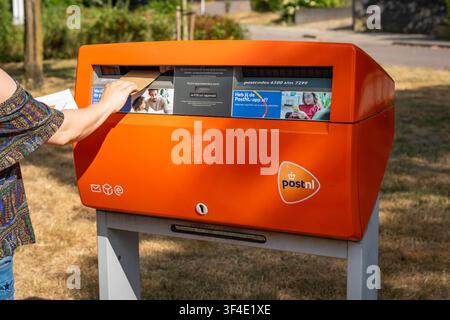 Ede, Pays-Bas, 25.07.2026, Envoi d'une lettre dans une boîte postale orange PostNL, boîte postale de rue du service postal néerlandais Banque D'Images