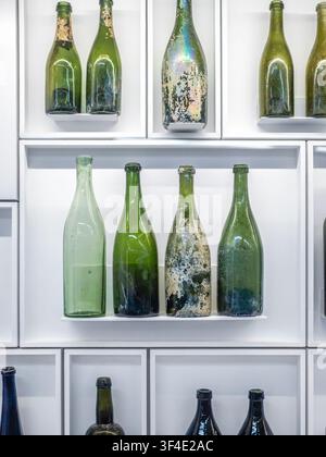 Anciennes bouteilles de vin en verre vert vieilli européennes du XVIIIe siècle exposées dans des étagères encadrées de blanc. Banque D'Images
