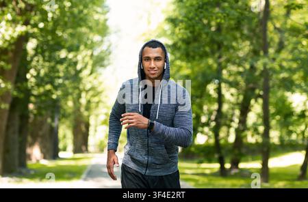 Entraînement d'athlète noir souriant pour le marathon au parc vert en été Banque D'Images