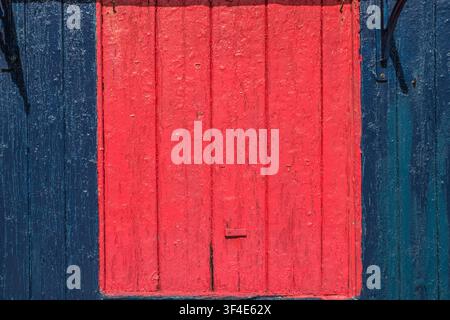 Une porte à battants rouge sur un abri en bois bleu avec une peinture écaillée Banque D'Images